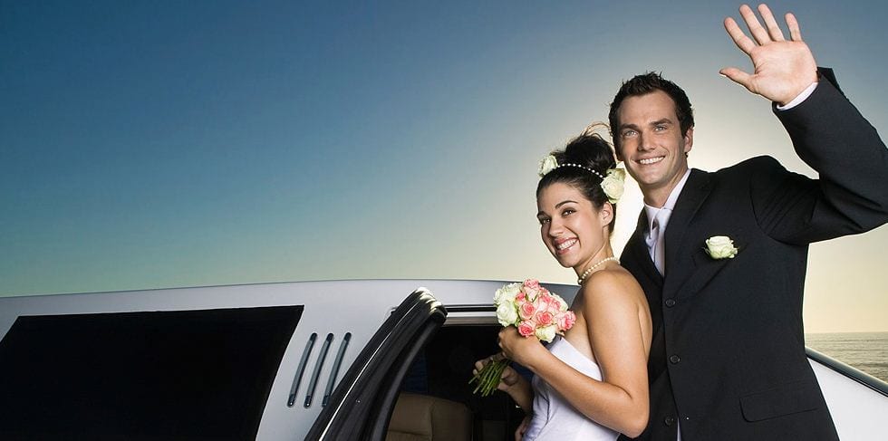 wedding couple in front of limo waving